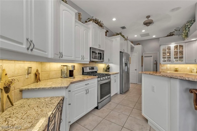 kitchen featuring white cabinets, appliances with stainless steel finishes, tasteful backsplash, light tile patterned flooring, and light stone counters