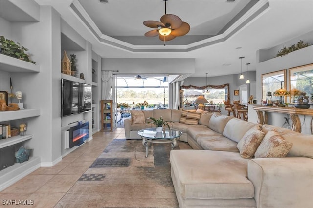 tiled living room with ceiling fan, a raised ceiling, built in features, and ornamental molding