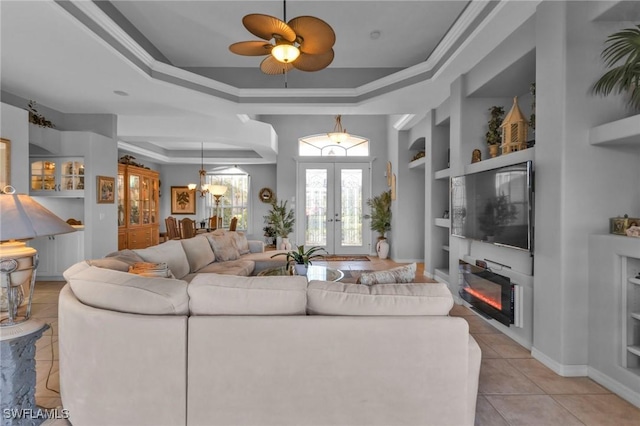 living room with built in shelves, ceiling fan, french doors, a raised ceiling, and ornamental molding