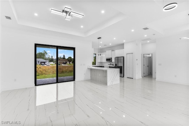 kitchen featuring pendant lighting, a tray ceiling, white cabinetry, kitchen peninsula, and stainless steel appliances