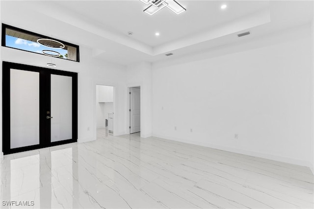 empty room featuring a tray ceiling and french doors