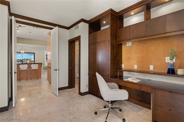 office with built in desk, ornamental molding, and an inviting chandelier