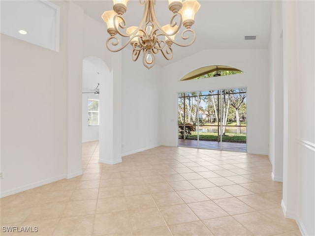 tiled empty room featuring ceiling fan with notable chandelier, vaulted ceiling, and a healthy amount of sunlight