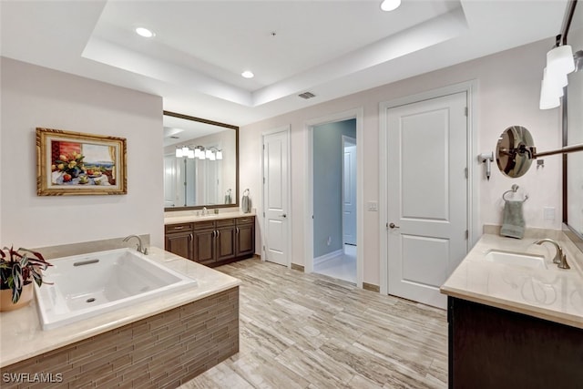 bathroom featuring vanity, tiled bath, and a raised ceiling