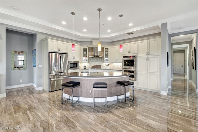 kitchen featuring wall chimney exhaust hood, hanging light fixtures, tasteful backsplash, a center island with sink, and appliances with stainless steel finishes