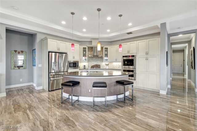 kitchen with a breakfast bar, decorative light fixtures, a kitchen island with sink, stainless steel appliances, and wall chimney exhaust hood