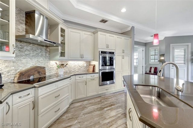 kitchen with white cabinetry, backsplash, sink, and wall chimney range hood