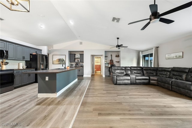 living room with light wood-type flooring, vaulted ceiling, ceiling fan, and sink