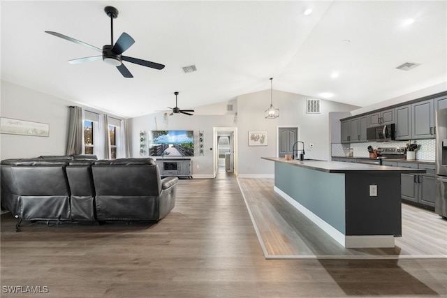 kitchen featuring hardwood / wood-style floors, lofted ceiling, backsplash, a kitchen island with sink, and stainless steel appliances