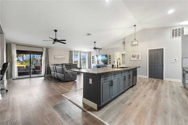 kitchen featuring dishwasher, a kitchen island with sink, sink, vaulted ceiling, and decorative light fixtures