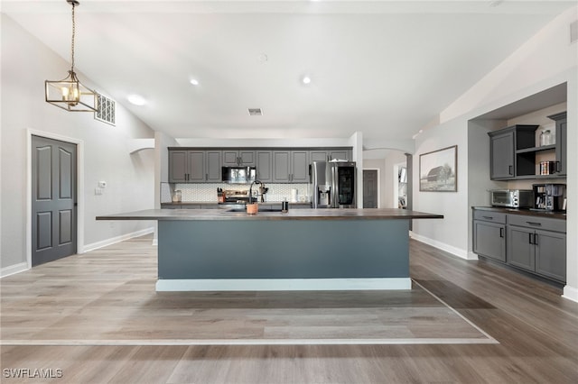 kitchen with stainless steel refrigerator with ice dispenser, gray cabinetry, lofted ceiling, and an island with sink