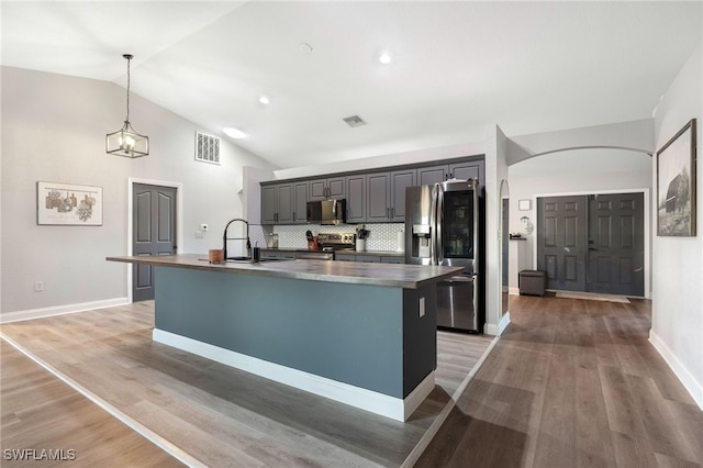 kitchen with decorative backsplash, appliances with stainless steel finishes, sink, a center island with sink, and decorative light fixtures