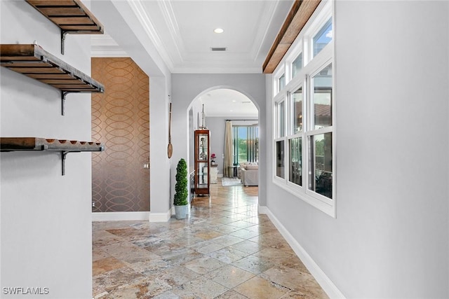 hall with an accent wall, baseboards, arched walkways, and crown molding