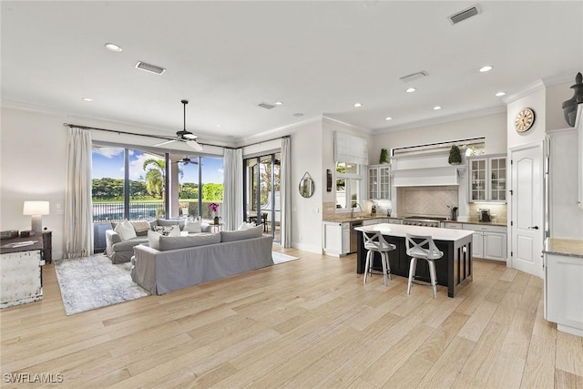 living room with light wood-style flooring, visible vents, and crown molding