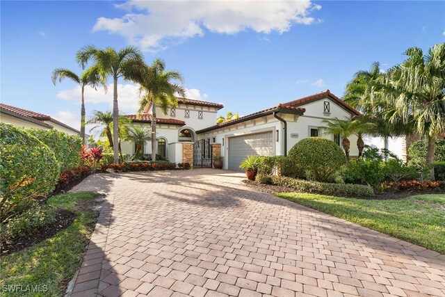 mediterranean / spanish-style house with an attached garage, a tiled roof, decorative driveway, and stucco siding