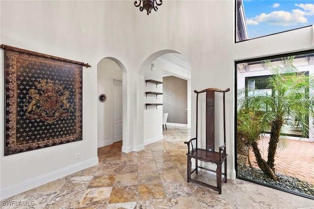 foyer entrance featuring arched walkways, stone finish floor, a towering ceiling, and baseboards