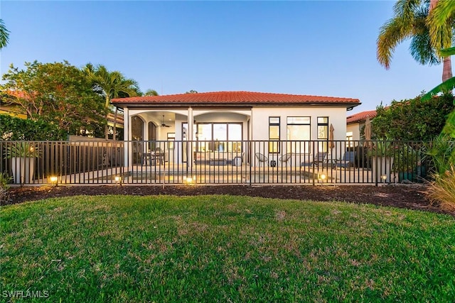 rear view of house featuring stucco siding, a lawn, a ceiling fan, a patio area, and fence