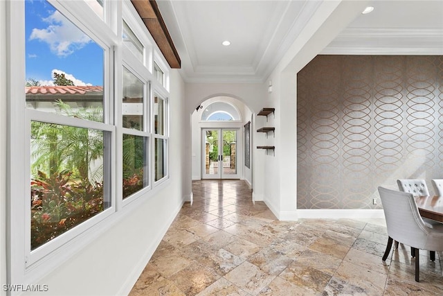 hall featuring stone tile floors, an accent wall, baseboards, ornamental molding, and wallpapered walls