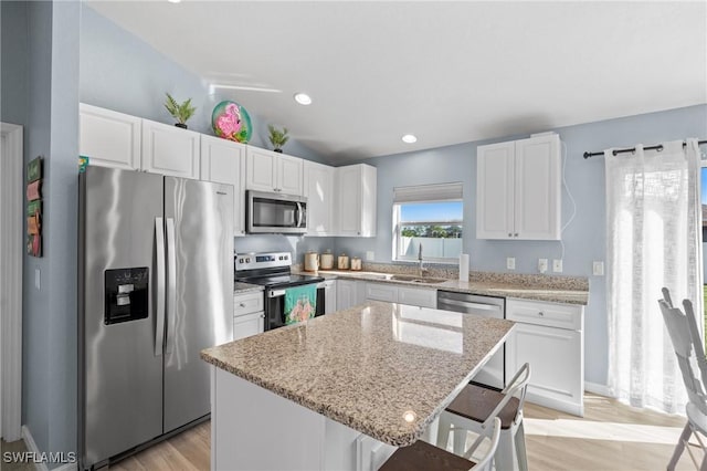 kitchen with appliances with stainless steel finishes, a kitchen breakfast bar, light stone counters, a kitchen island, and white cabinetry