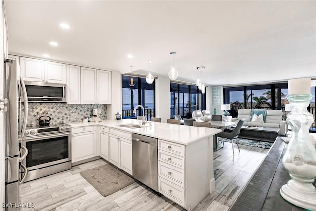 kitchen with sink, hanging light fixtures, stainless steel appliances, kitchen peninsula, and white cabinets