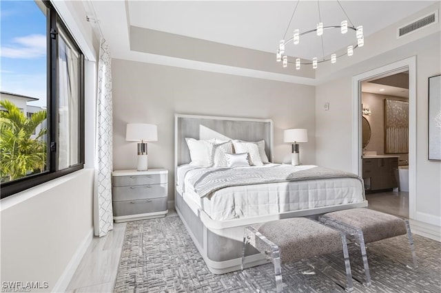 bedroom with a tray ceiling, light wood-type flooring, connected bathroom, and multiple windows