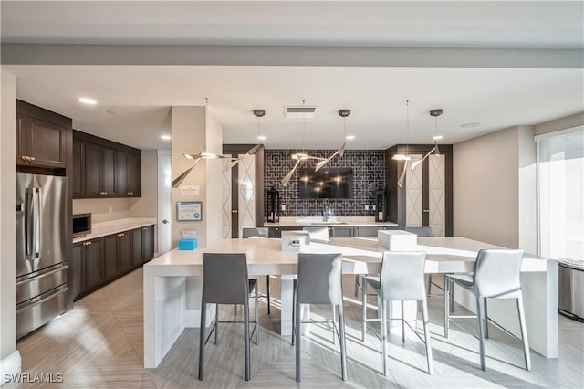 kitchen featuring pendant lighting, a large island, appliances with stainless steel finishes, dark brown cabinets, and a kitchen bar