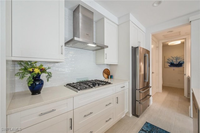 kitchen with backsplash, wall chimney exhaust hood, stainless steel appliances, white cabinets, and light tile patterned flooring