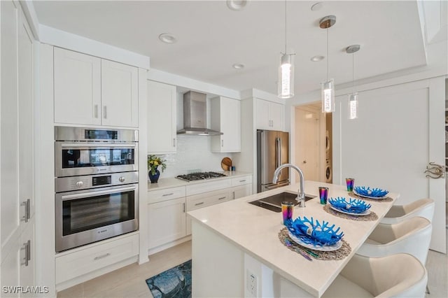 kitchen featuring white cabinets, wall chimney range hood, stainless steel appliances, and tasteful backsplash