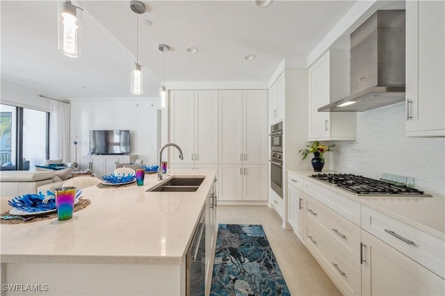 kitchen with a kitchen island with sink, white cabinets, wall chimney range hood, sink, and appliances with stainless steel finishes