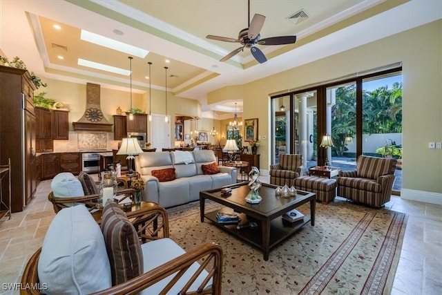 living room with ceiling fan with notable chandelier, a tray ceiling, a skylight, and ornamental molding