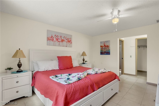 bedroom with a walk in closet, a textured ceiling, ceiling fan, light tile patterned floors, and a closet