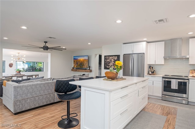 kitchen featuring backsplash, white cabinets, wall chimney range hood, appliances with stainless steel finishes, and a breakfast bar area