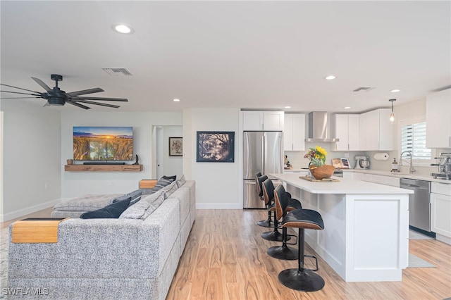 kitchen with a breakfast bar, stainless steel appliances, wall chimney range hood, a center island, and white cabinetry