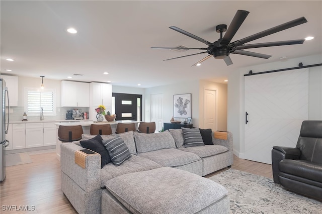 living room with a barn door, ceiling fan, sink, and light hardwood / wood-style floors