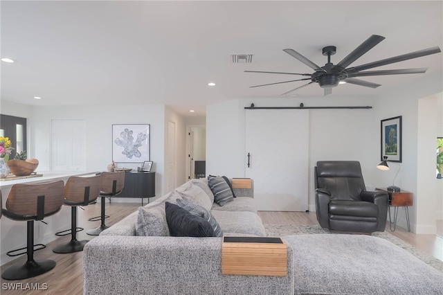 living room featuring ceiling fan, a barn door, and light hardwood / wood-style flooring