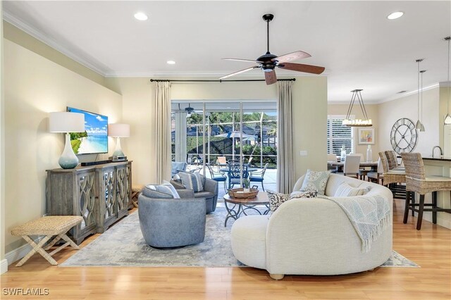 living room featuring hardwood / wood-style flooring, ceiling fan with notable chandelier, sink, and crown molding