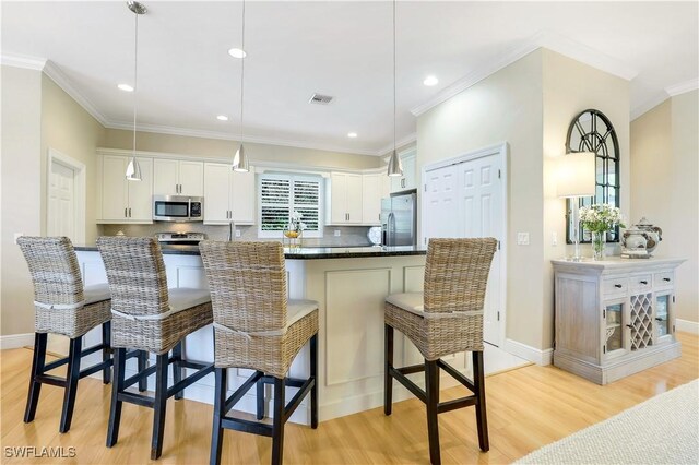 kitchen featuring stainless steel appliances, light wood-style flooring, decorative backsplash, white cabinetry, and a kitchen bar