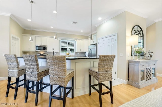 kitchen featuring a breakfast bar, light wood-style flooring, white cabinetry, crown molding, and appliances with stainless steel finishes