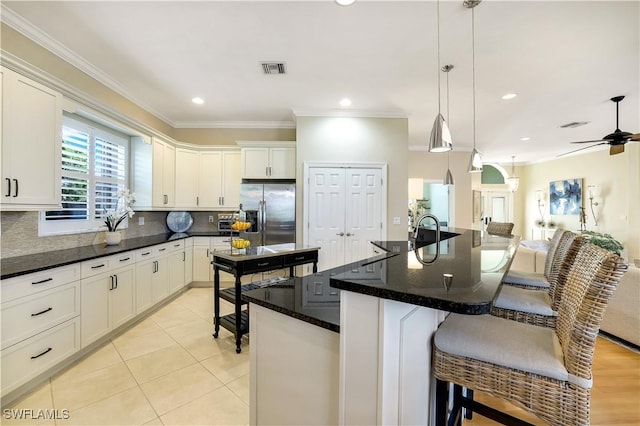 kitchen featuring stainless steel fridge with ice dispenser, tasteful backsplash, a breakfast bar, crown molding, and a ceiling fan