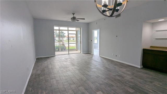 spare room featuring dark wood-type flooring and ceiling fan with notable chandelier