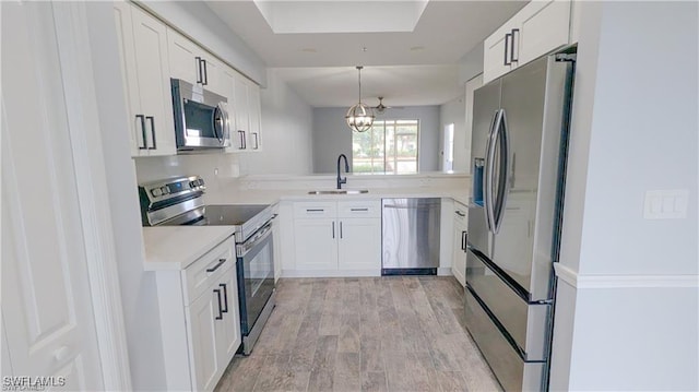 kitchen with stainless steel appliances, sink, pendant lighting, light hardwood / wood-style flooring, and white cabinets