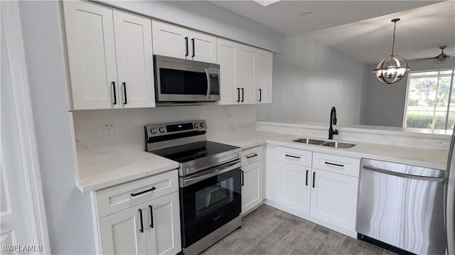 kitchen featuring sink, hanging light fixtures, stainless steel appliances, light hardwood / wood-style floors, and white cabinets