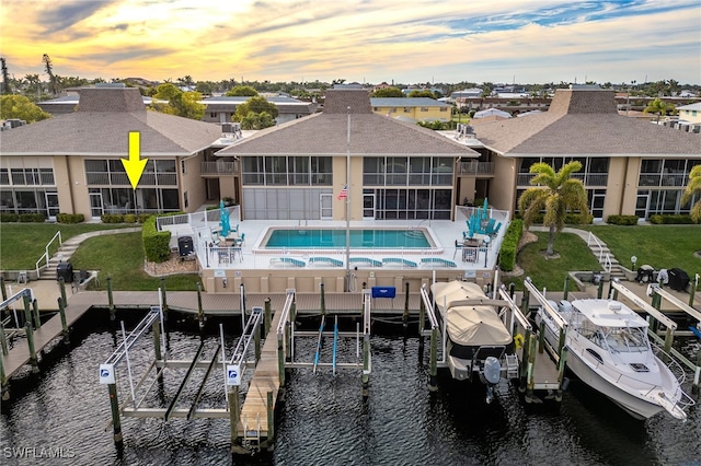 back house at dusk featuring a patio area, a water view, and a community pool