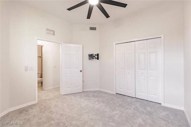 unfurnished bedroom featuring a high ceiling, a closet, light colored carpet, and ceiling fan