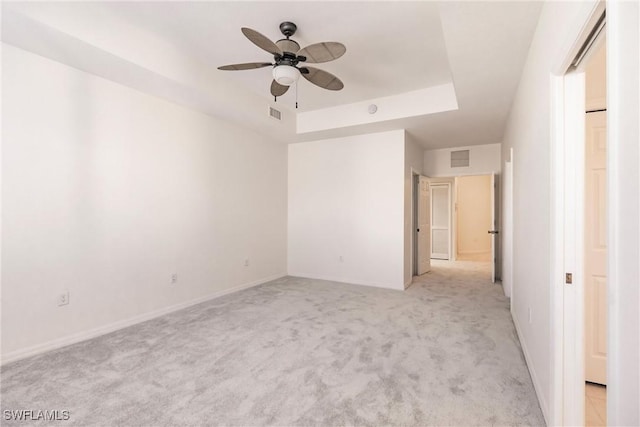 spare room with light colored carpet, a raised ceiling, and ceiling fan