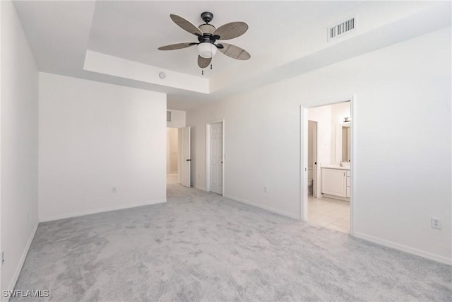 unfurnished bedroom with light carpet, a tray ceiling, ensuite bath, and ceiling fan