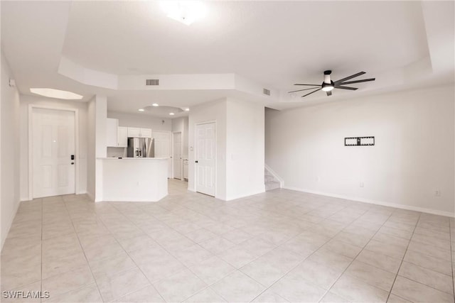 unfurnished living room with ceiling fan, a raised ceiling, and light tile patterned floors