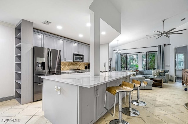 kitchen with appliances with stainless steel finishes, light stone counters, gray cabinetry, a kitchen island, and lofted ceiling