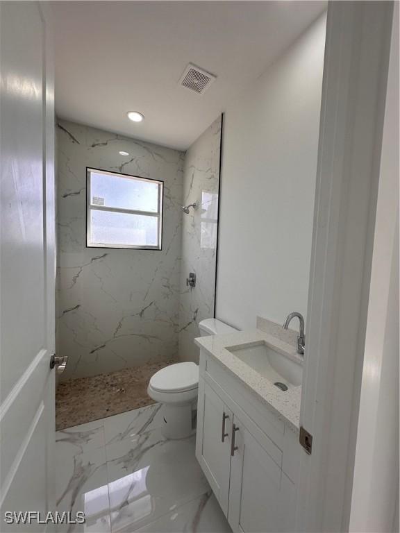 bathroom featuring vanity, toilet, and a tile shower