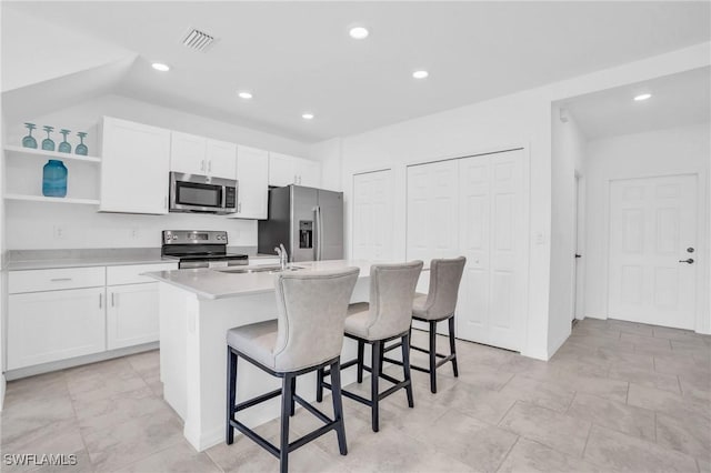 kitchen featuring white cabinetry, an island with sink, vaulted ceiling, a kitchen bar, and appliances with stainless steel finishes